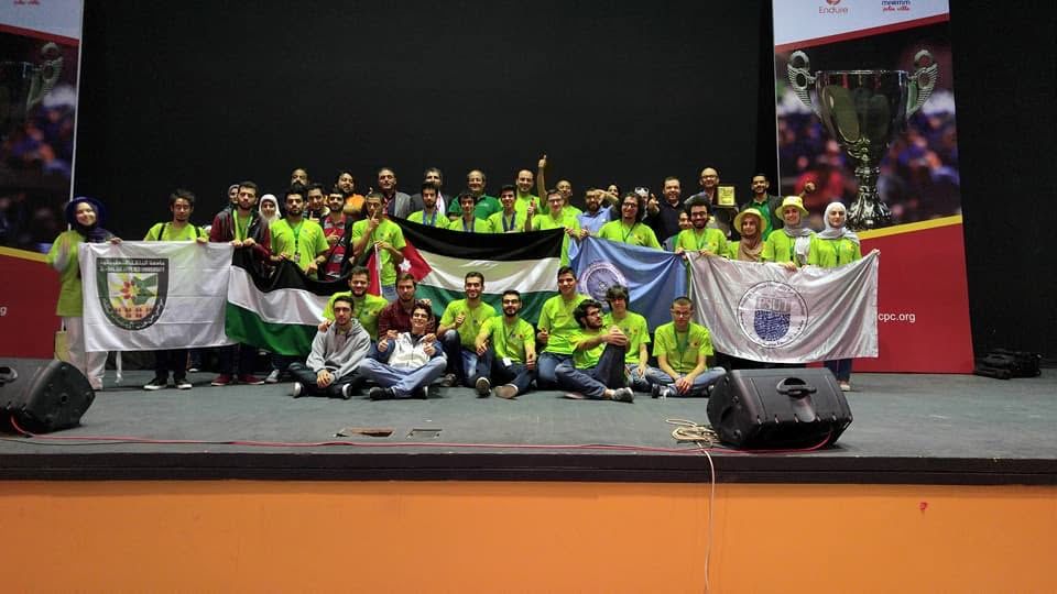 JCPC group photo on stage with the Jordanian flag and university banners